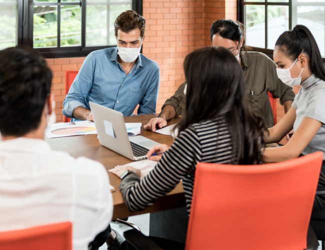 Group of asian and caucasian business person team meeting and brainstorm in meeting room after office reopen, they wear protective face mask as new normal practice to prevent coronavirus infection.